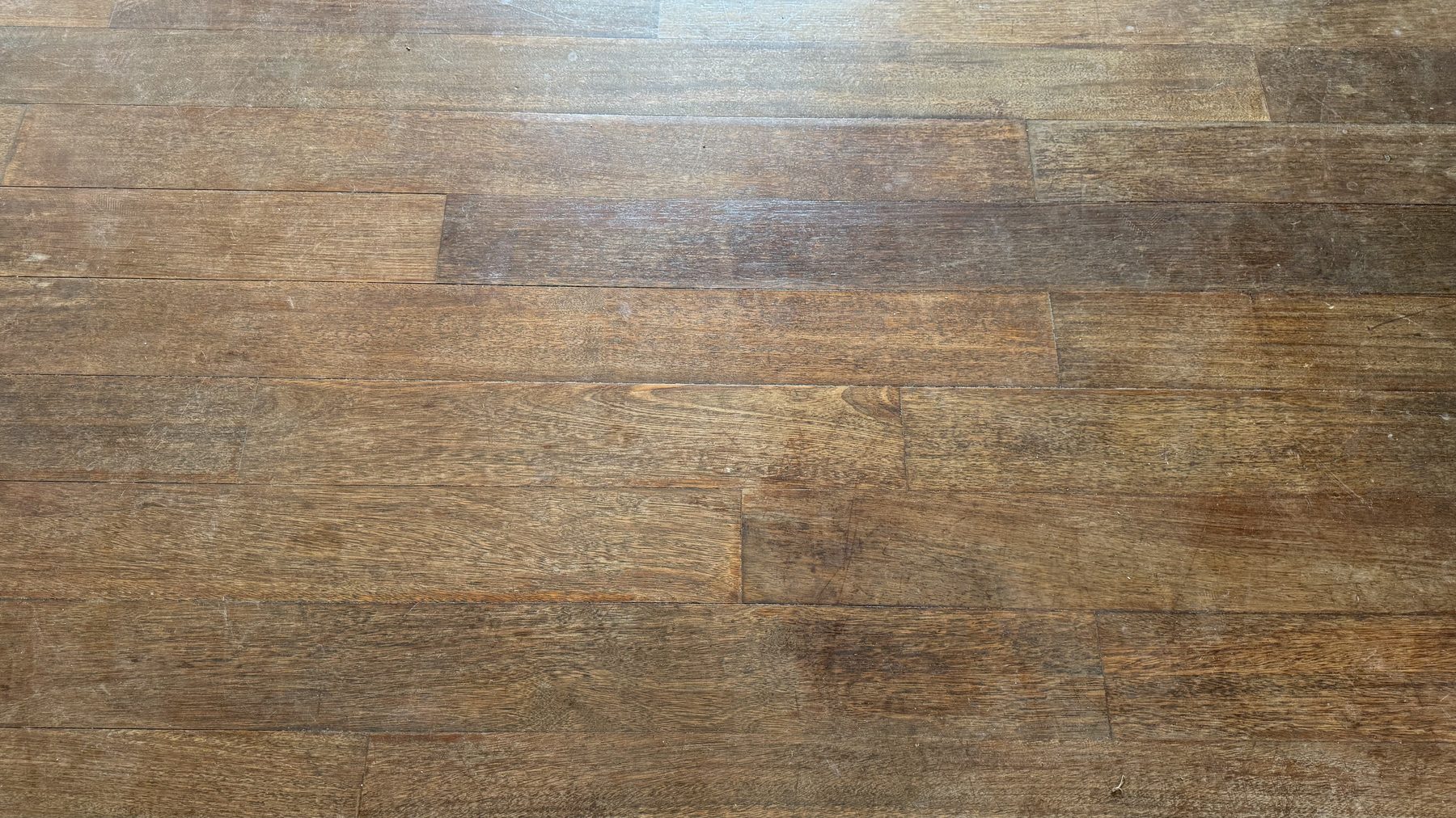 Avant : Gros plan d'un parquet merbau : à gauche rayé et terni, à droite poncé et verni