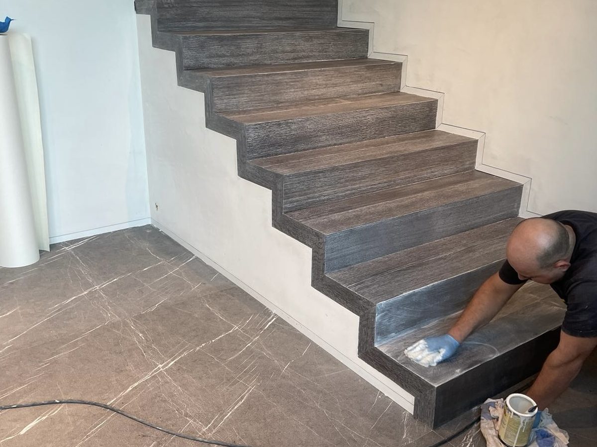 Escalier habillé de bois foncé, artisan en train de finir une marche