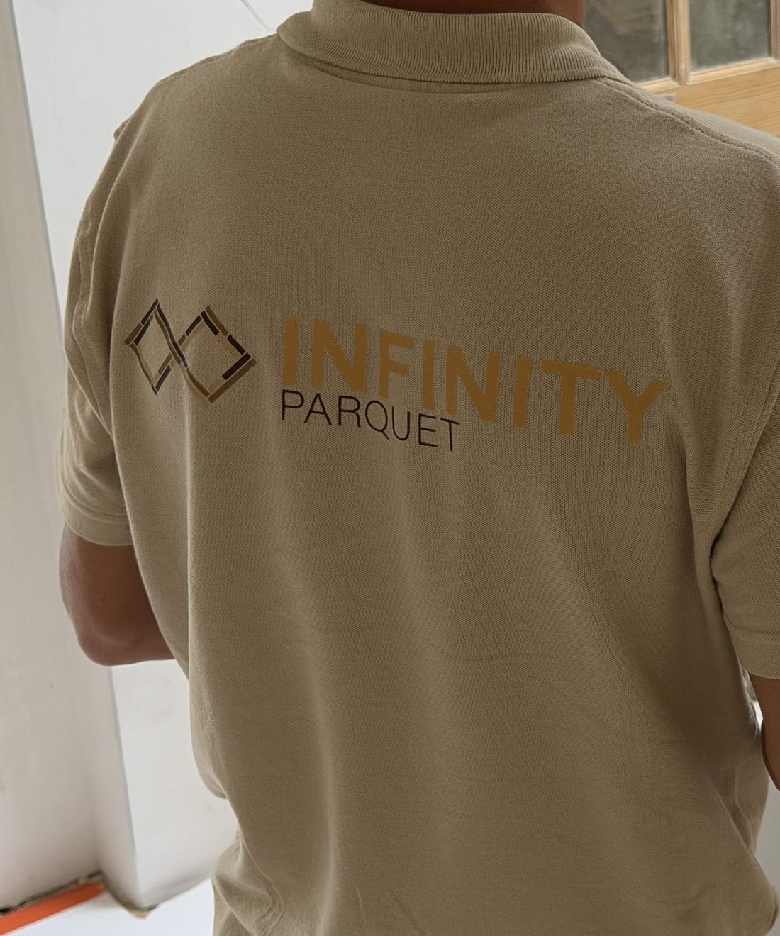 Artisan Infinity Parquet de dos sur un chantier, polo de l'entreprise et plans posés derrière lui