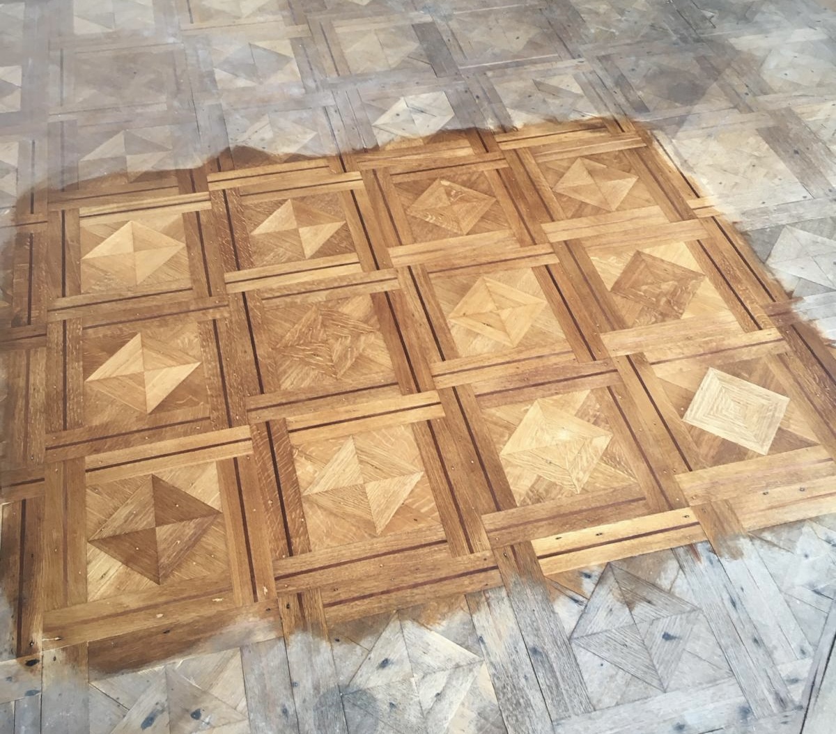 Parquet de Versailles à panneaux marquetés, une partie poncée et vitrifiée, le reste encore brut